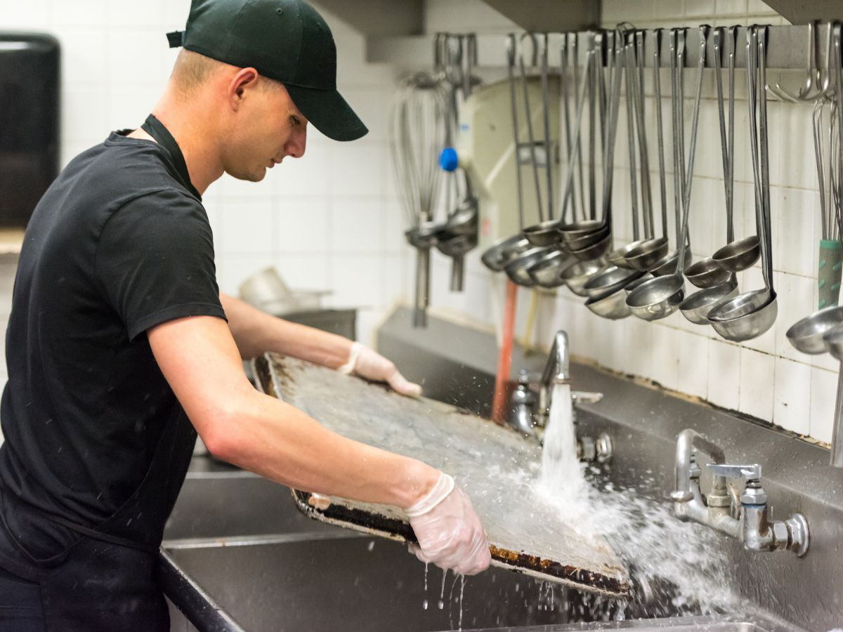 A dishwasher at Tasty Treat Restaurant diligently at work, exemplifying the dedication and efficiency essential for maintaining kitchen hygiene and ensuring a seamless dining experience